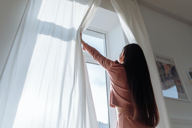 Woman opening curtains as a healthy morning habit